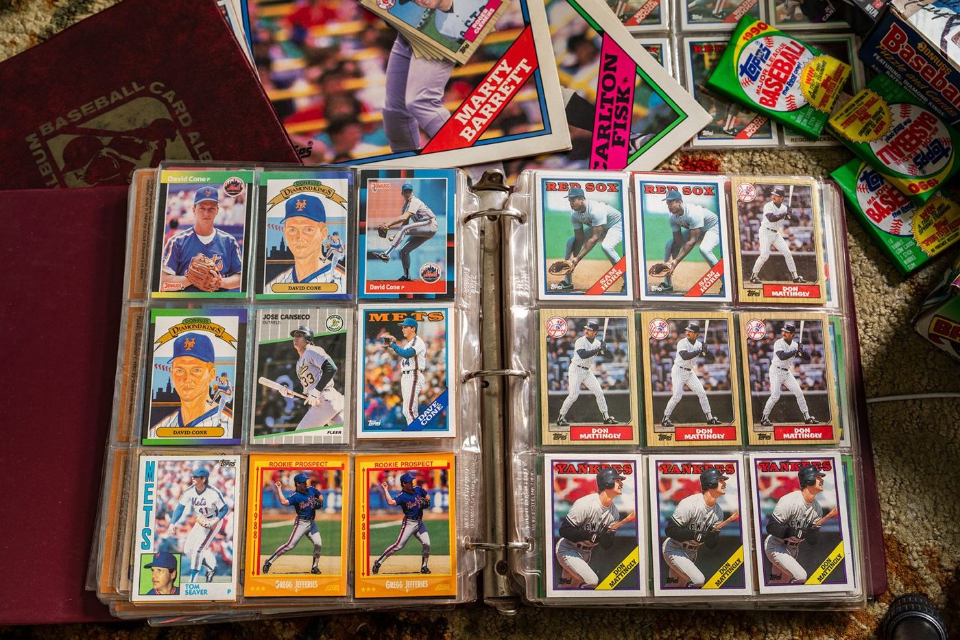 A late-1980s baseball card binder lying open, nine-pocket pages full of cards, wax packs around it